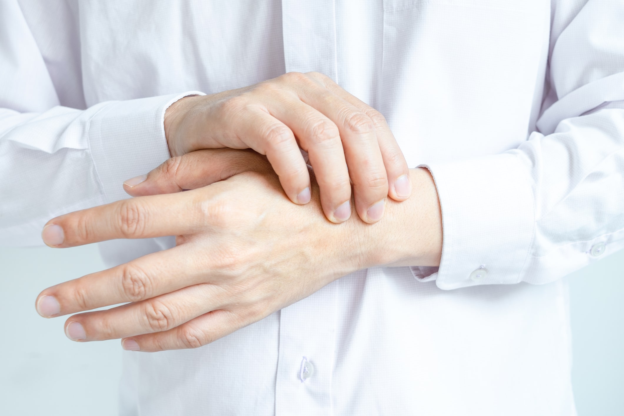 Eine Person in einem weißen Hemd, die ihr Handgelenk mit der anderen Hand hält und reibt, als ob sie Beschwerden oder Schmerzen durch Tendovaginitis De Quervain hat.