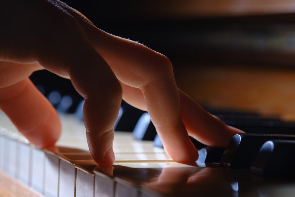 Eine Nahaufnahme einer Hand, die auf Klaviertasten spielt, wobei die Finger bei schwachem Licht mehrere Tasten drücken, um den Fokus und die Präzision einzufangen, die in der Musikerbehandlung wichtig sind.